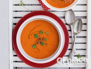 Two bowls of cream of tomato soup with fresh basil on a wooden tray